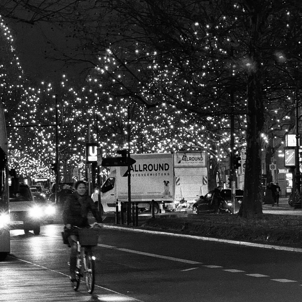 Cyclist crossing a Berlin street beneath illuminated trees at night
